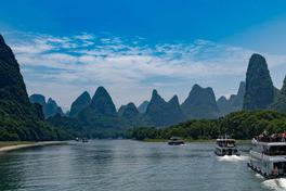 Karst limestone peaks lining the Li River near Guilin with tour boats on the water — Photo: xiquinhosilva / CC BY 2.0 via Wikimedia Commons