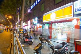 A Shanghai back-street food row at night, lit noodle shop and snack store signs — Photo: Михаил Лазарев / CC BY 2.0 via Wikimedia Commons